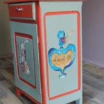 Petit meuble bas fermé pris de droite, après rénovation, avec deux illustrations peintes à la main sur le thème Alice au pays des merveilles