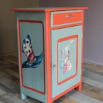 Petit meuble bas fermé de 3/4, après rénovation, avec illustrations peintes à la main sur deux faces, sur le thème Alice au pays des merveilles